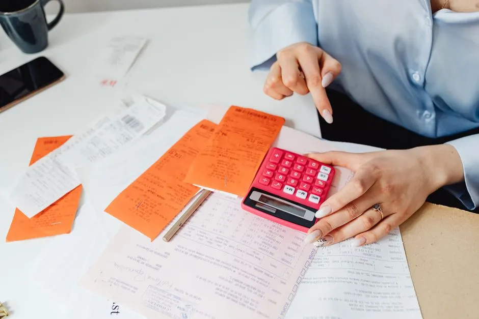 Mains tenant une calculatrice au-dessus de justificatifs de frais et d'un formulaire fiscal, pour calculer la TVA récupérable