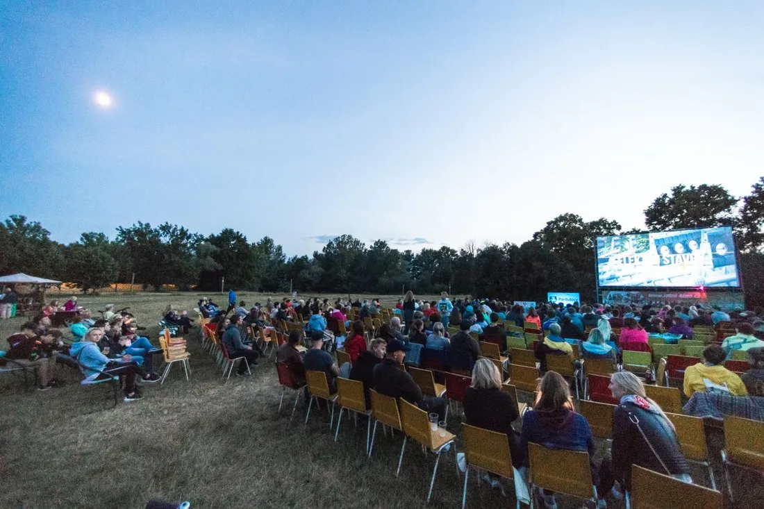 Public installé en plein air à la tombée de la nuit devant un grand écran de cinéma lors d'une projection de festival