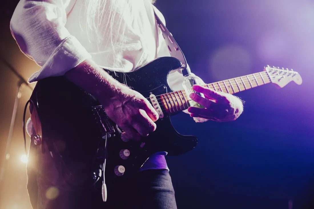Guitariste jouant de la guitare electrique sur scene sous des lumieres violettes, ambiance concert de blues du festival