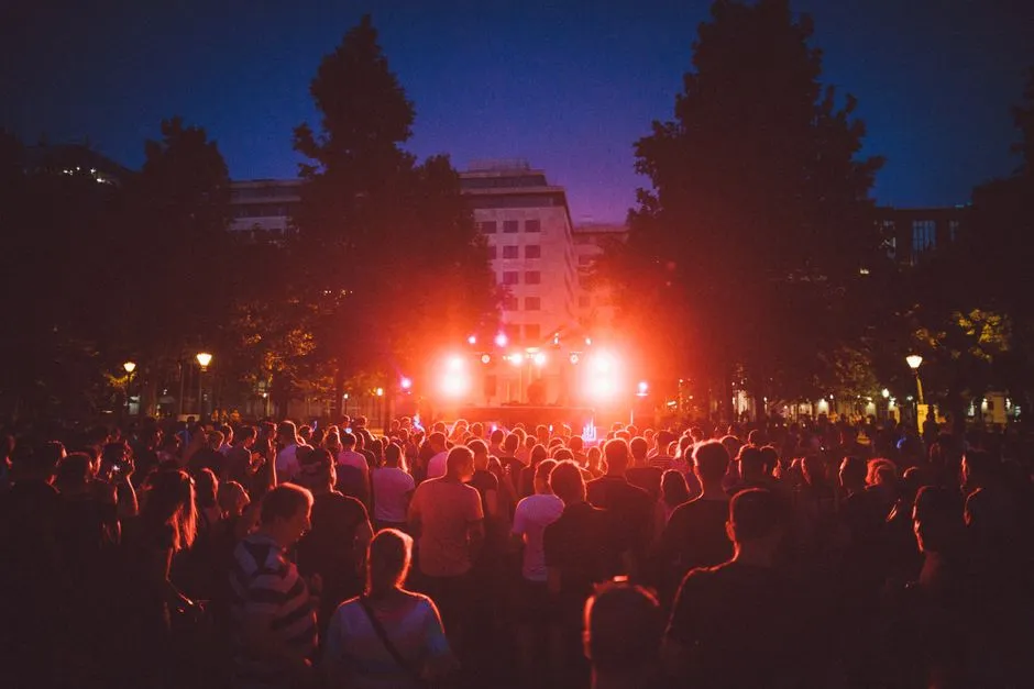 Concert en plein air le soir : une foule rassemblée devant une scène éclairée au milieu des arbres d'une place, ambiance typique de la Fête de la musique