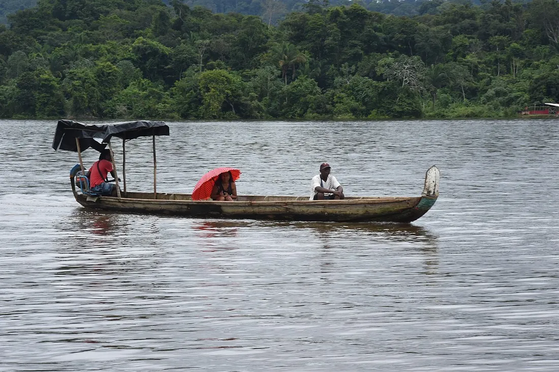 Pirogue traditionnelle transportant des passagers sur le fleuve Maroni, bordé par la forêt amazonienne en Guyane