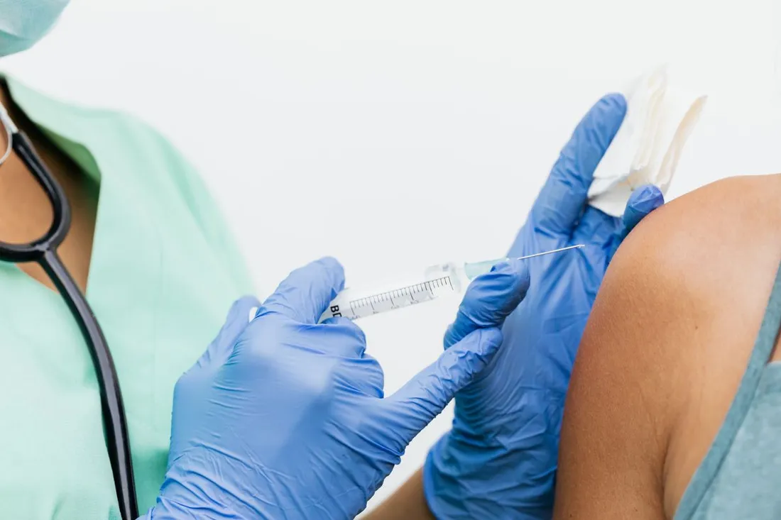 Injection d'un vaccin dans le bras d'une personne par un soignant ganté, illustrant la vaccination contre la fièvre jaune exigée pour entrer en Guyane