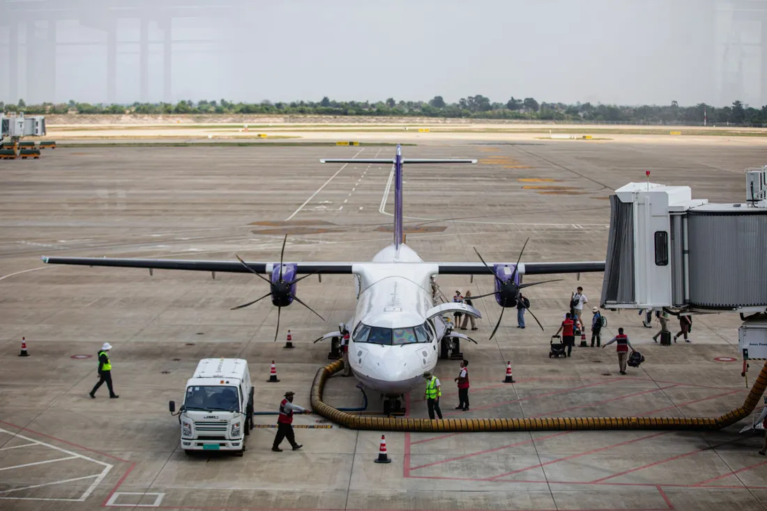 Avion de ligne à hélices stationné sur le tarmac, passerelle accostée, passagers descendant sur la piste et personnel d'escale en gilets fluorescents