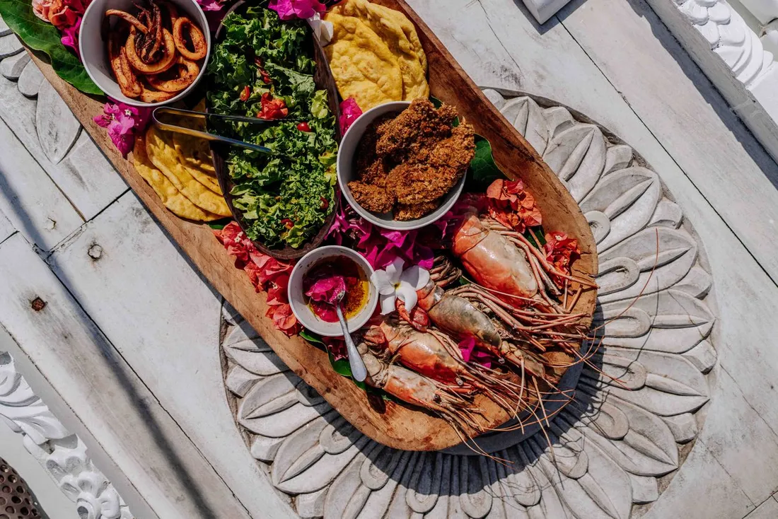 Plateau de fruits de mer et spécialités créoles servi sur une planche en bois : grosses crevettes, accras, salade et chips de banane plantain