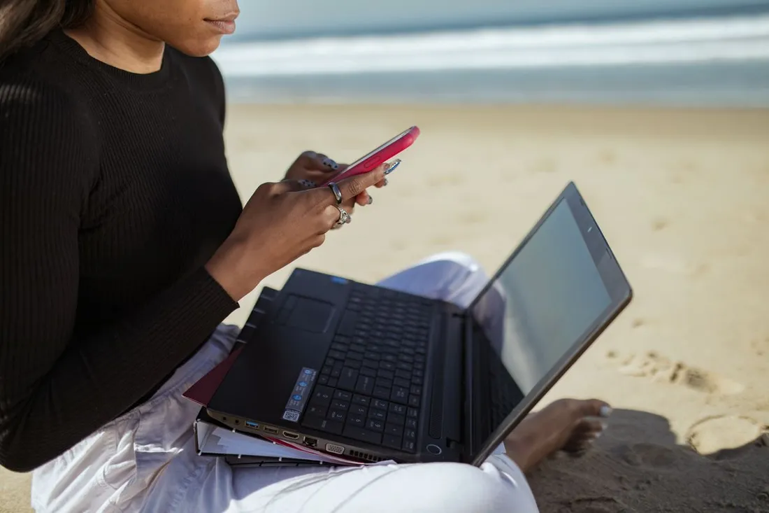 Personne gérant à distance avec un ordinateur portable et un smartphone en bord de mer, illustration de la gestion locative depuis la métropole