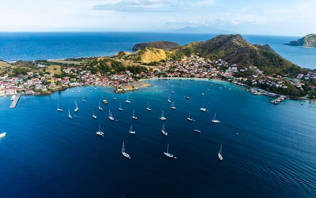 Vue aérienne de l'archipel des Saintes en Guadeloupe, avec voiliers ancrés dans la baie de Terre-de-Haut et le bourg au pied des collines