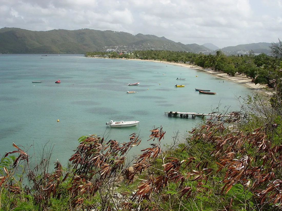 Plage de Sainte-Anne en Martinique, baie aux eaux turquoise avec petits bateaux et collines verdoyantes