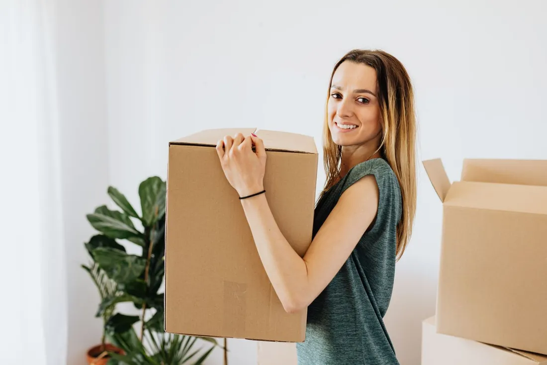 Jeune femme souriante portant un carton de déménagement dans son nouveau logement