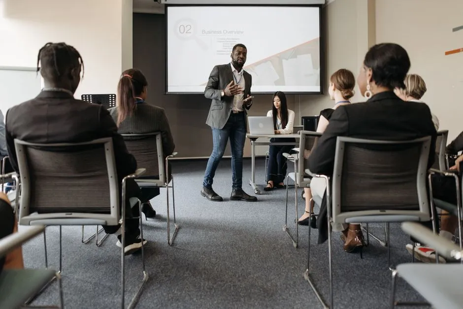 Un formateur debout devant un écran de projection anime une session face à un groupe de participants assis dans une salle de formation