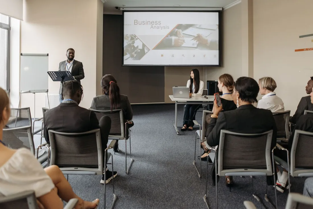 Groupe de professionnels assis en seminaire face a un intervenant et un ecran de projection dans une salle de formation