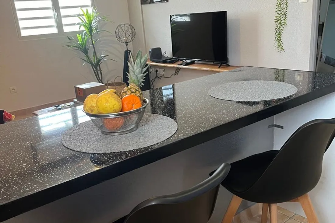 Mesa de refeição posta num apartamento em Caiena, com televisão e cortinas ao fundo