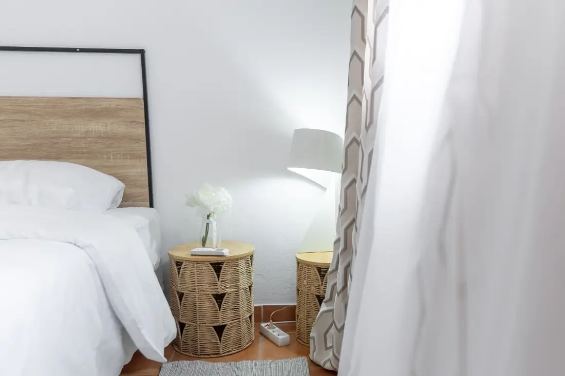 Chambre de la Casa Belas Artes : lit blanc à tête de bois clair, chevets en rotin et lampe allumée