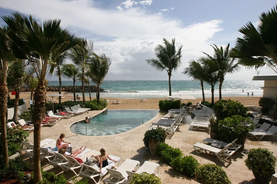 Piscine et transats d'un hotel balneaire en bord de plage aux Caraibes, palmiers et ocean en arriere-plan