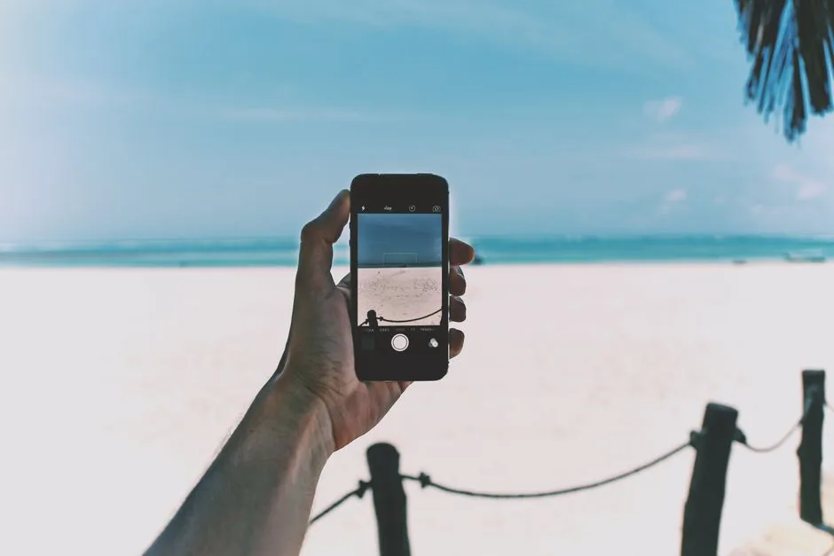 Smartphone tenu en main devant une plage tropicale de sable blanc et la mer