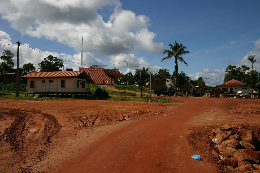 Vue du bourg d'Apatou en Guyane avec ses maisons sur pilotis, une piste en laterite rouge et des palmiers, village du Bas-Maroni