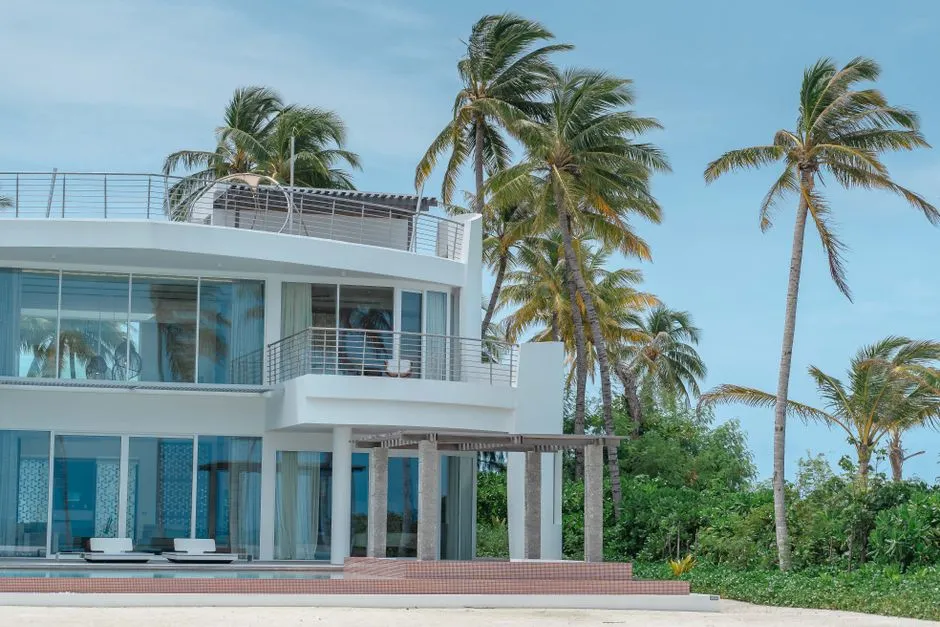 Villa moderne en bord de plage entourée de cocotiers, illustrant un bien de location saisonnière haut de gamme