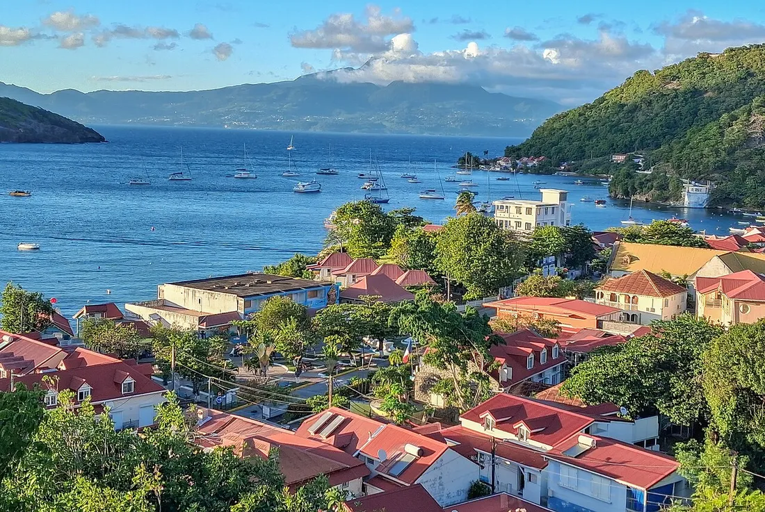 Vue sur les maisons aux toits rouges du bourg de Terre-de-Haut, aux Saintes, et sur la baie où mouillent des voiliers face à la Guadeloupe