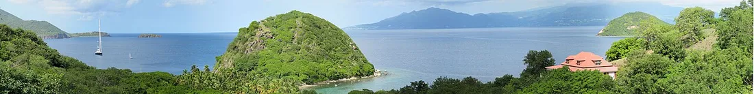 Panorama de l'île de Terre-de-Haut aux Saintes, près du rocher du Pain de Sucre, avec ses collines verdoyantes et des voiliers ancrés dans la baie