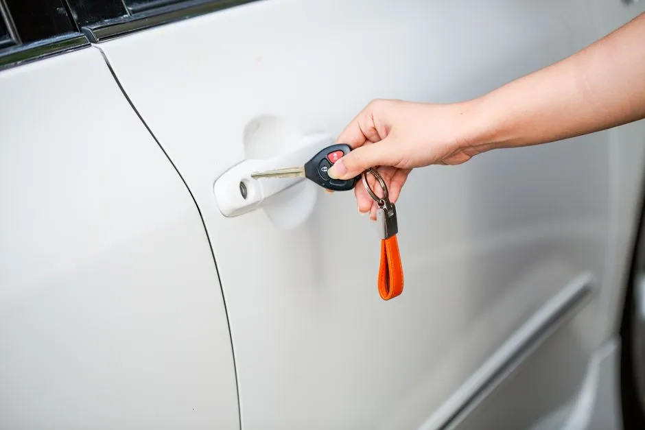 Main tendant une clé de voiture devant la portière d'un véhicule blanc, remise des clés de location