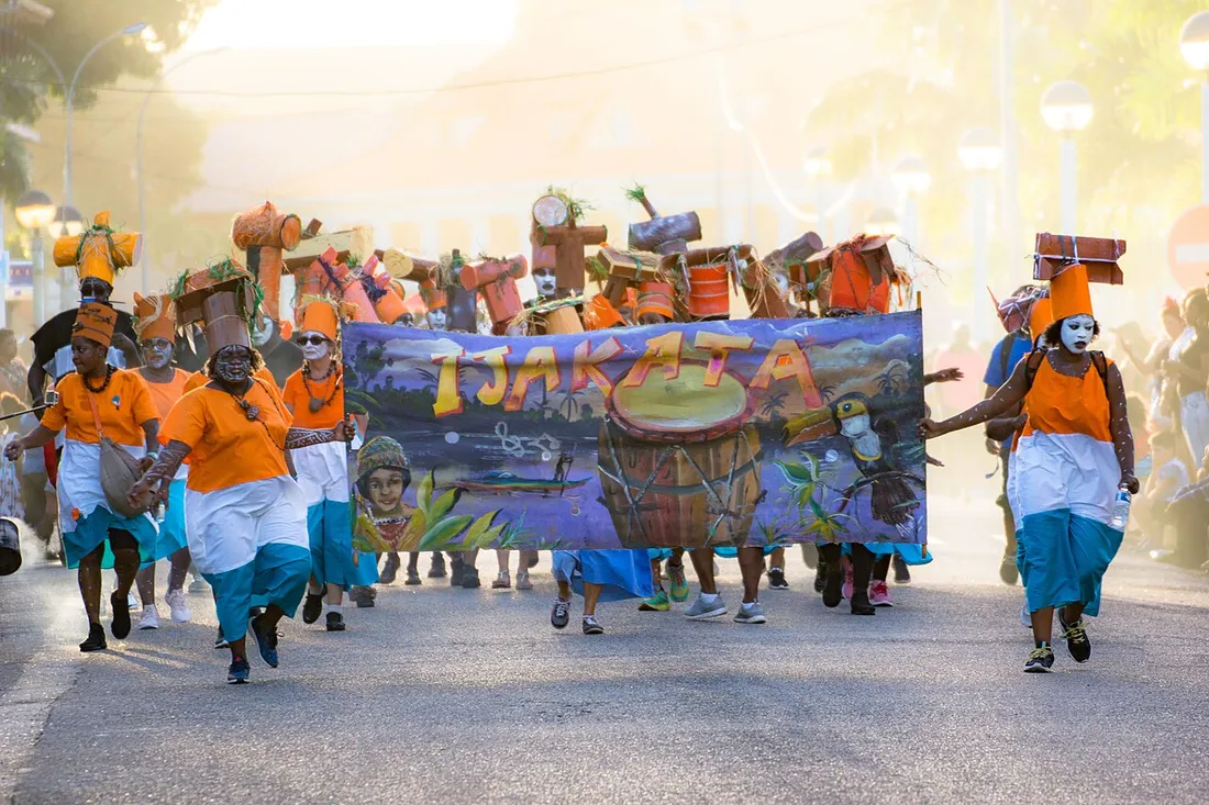 Parade du groupe Ijakata dans les rues de Cayenne pendant le carnaval de Guyane, avec costumes orange et grande banderole
