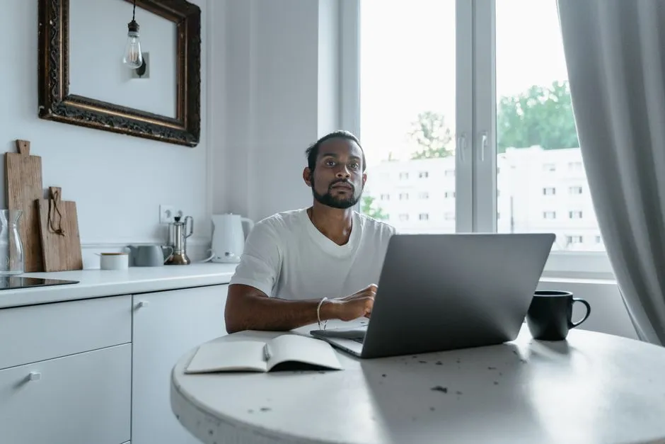 Collaborateur en déplacement professionnel travaillant sur son ordinateur portable dans la cuisine d'un appartement meublé