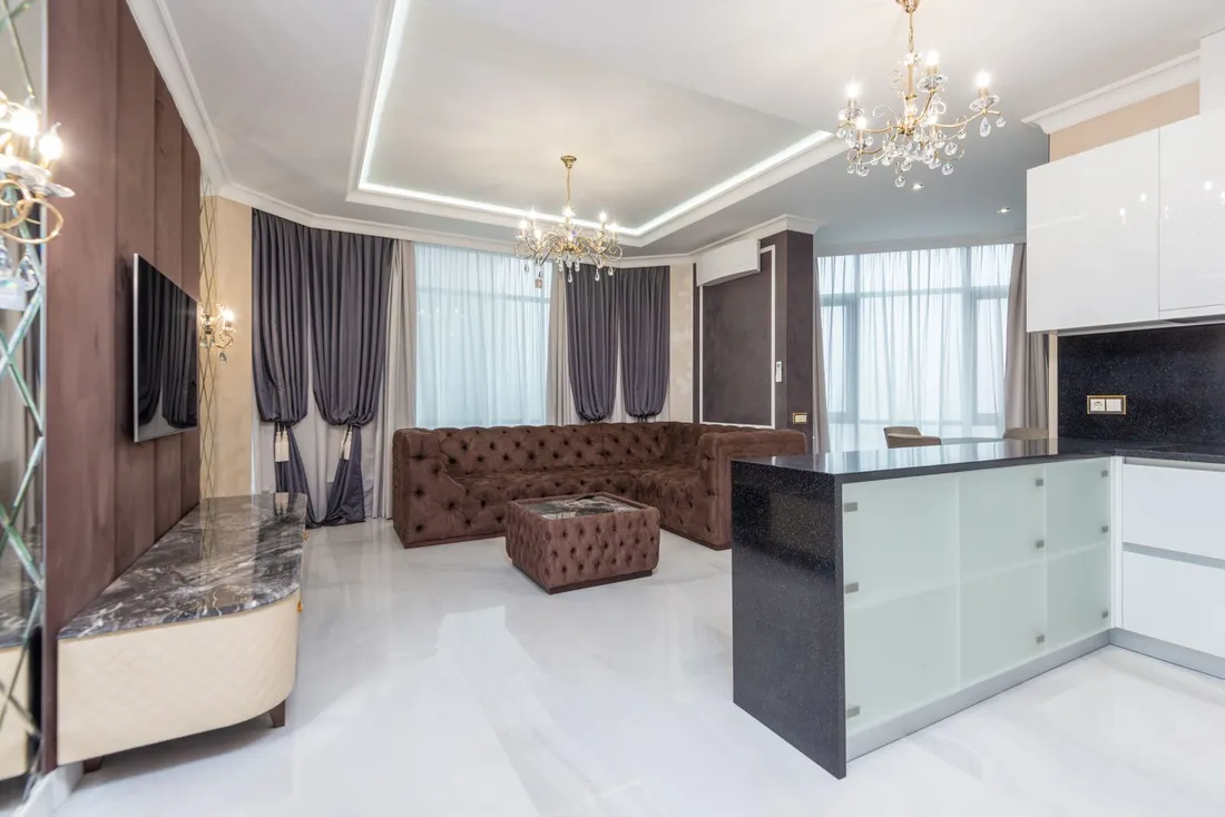 Salon spacieux et haut de gamme d'un appartement de standing avec lustres en cristal, canapé capitonné et cuisine ouverte, adapté à l'accueil d'un dirigeant en mission