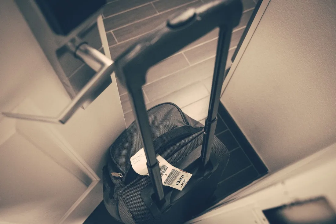 Valise cabine à roulettes posée à l'entrée d'un appartement, étiquette de bagage encore attachée, symbolisant l'arrivée d'un voyageur d'affaires en mission