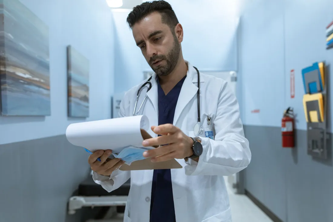 Médecin en blouse blanche avec stéthoscope consultant un dossier patient dans un couloir d'hôpital