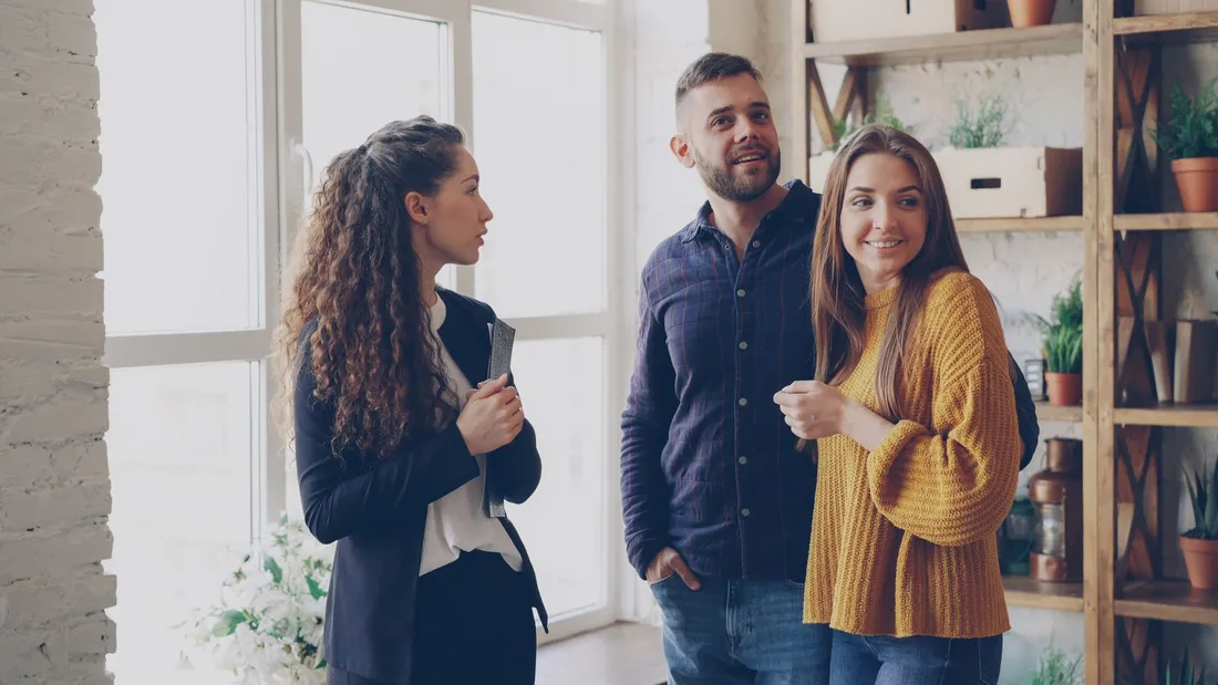 Une agente immobilière, dossier sous le bras, fait visiter un appartement clair à un couple