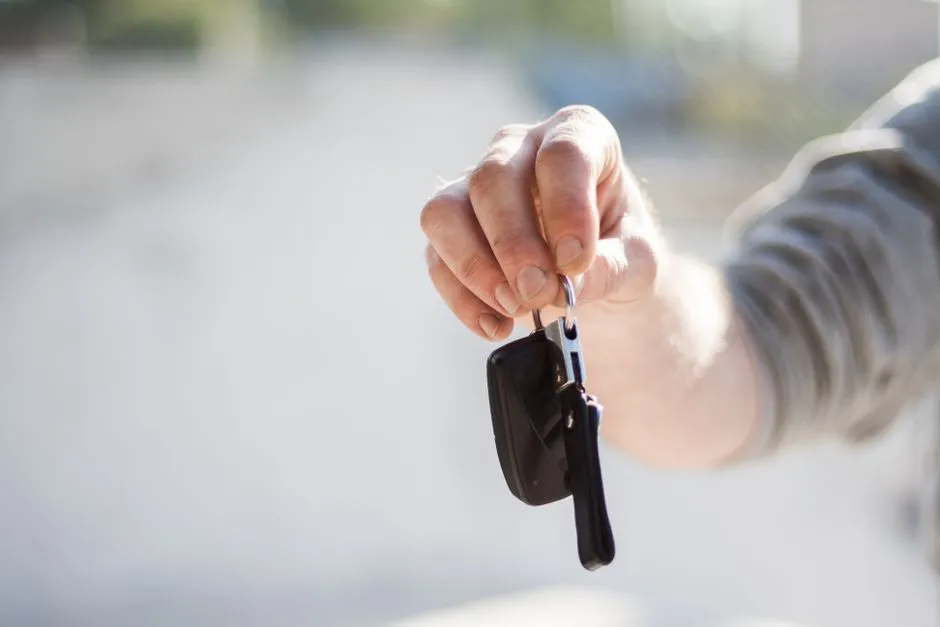 Main tendant une clé de voiture avec porte-clés, devant un arrière-plan de rue flou