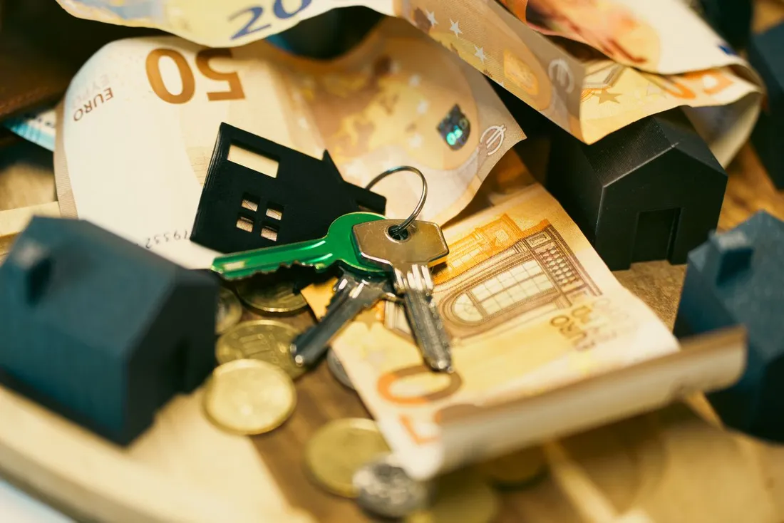 Trousseau de cles de logement pose sur des billets et pieces en euros, avec maisons miniatures