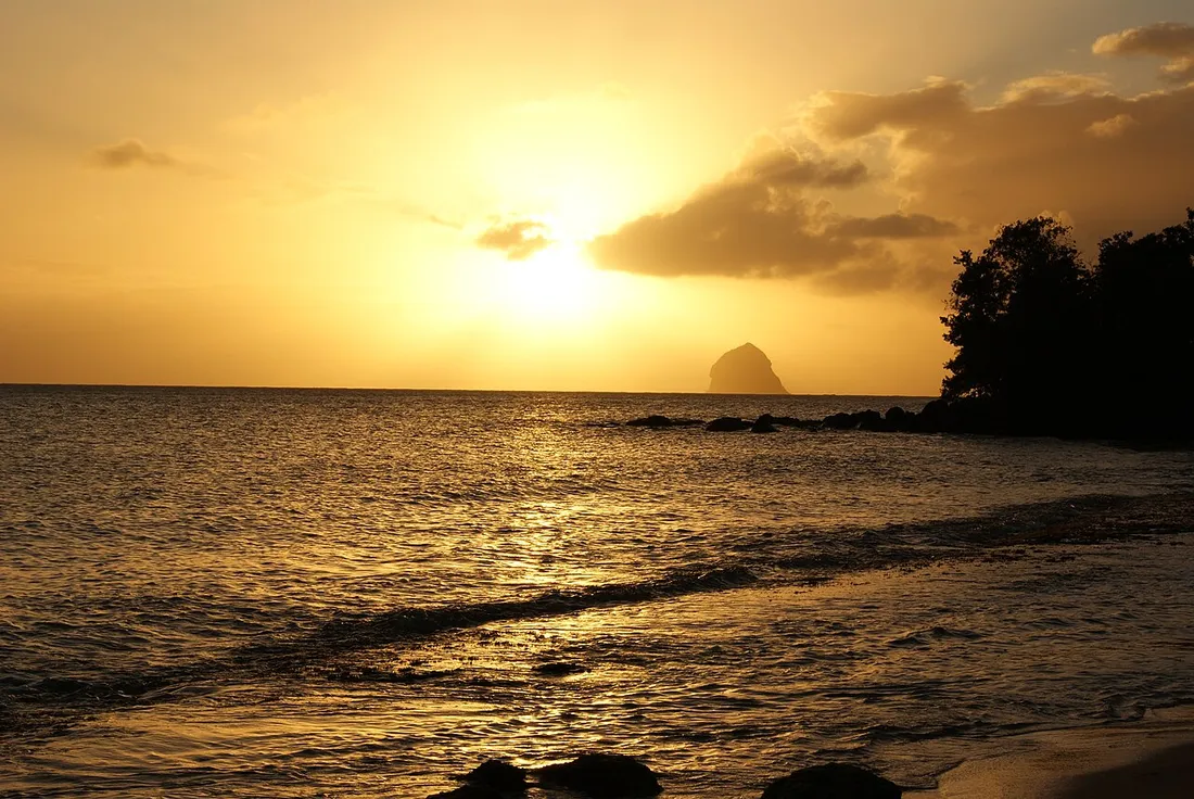 Coucher de soleil doré sur la mer avec la silhouette du Rocher du Diamant en Martinique, ambiance romantique de lune de miel