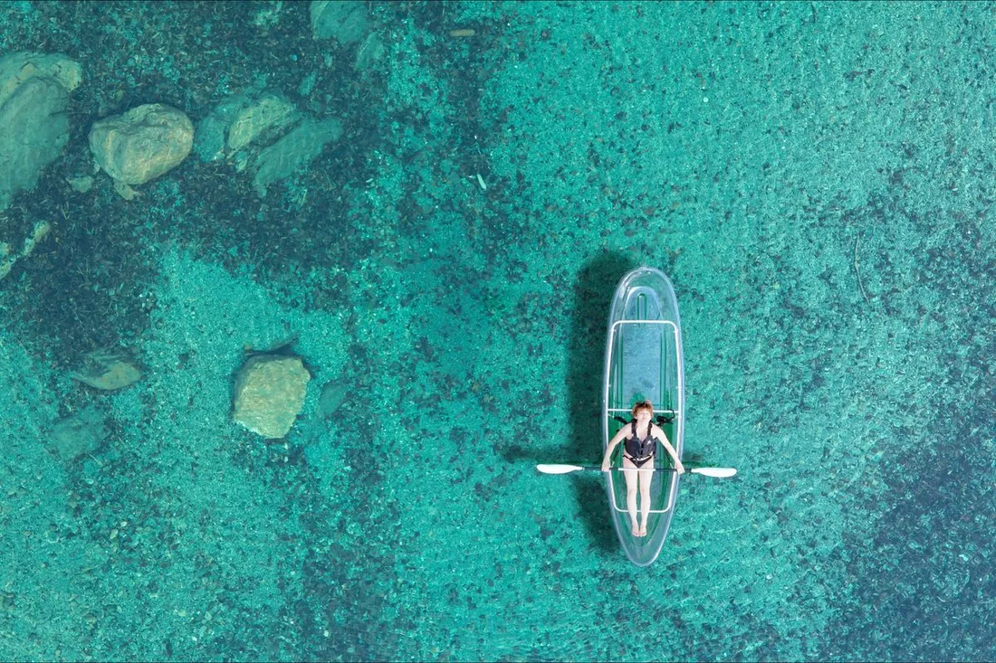 Vue aérienne d'un kayak transparent à fond clair glissant sur une eau turquoise peu profonde