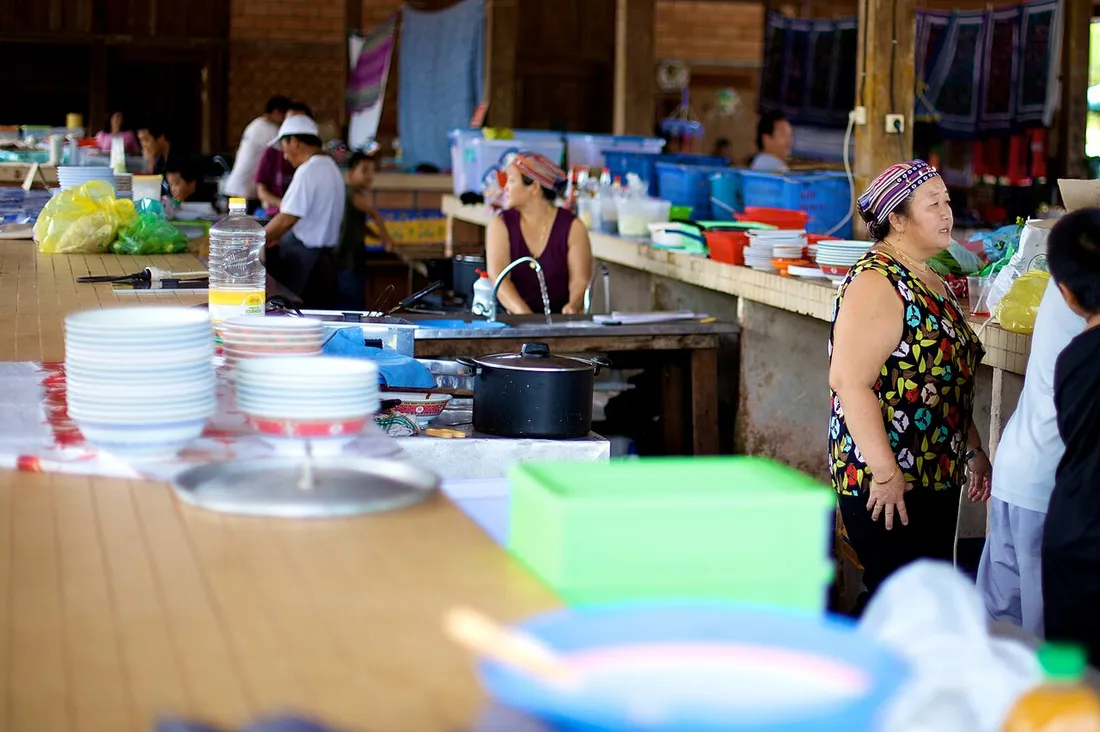 Femmes hmong en coiffe traditionnelle préparant et servant des plats derrière le comptoir du marché du dimanche de Cacao, en Guyane