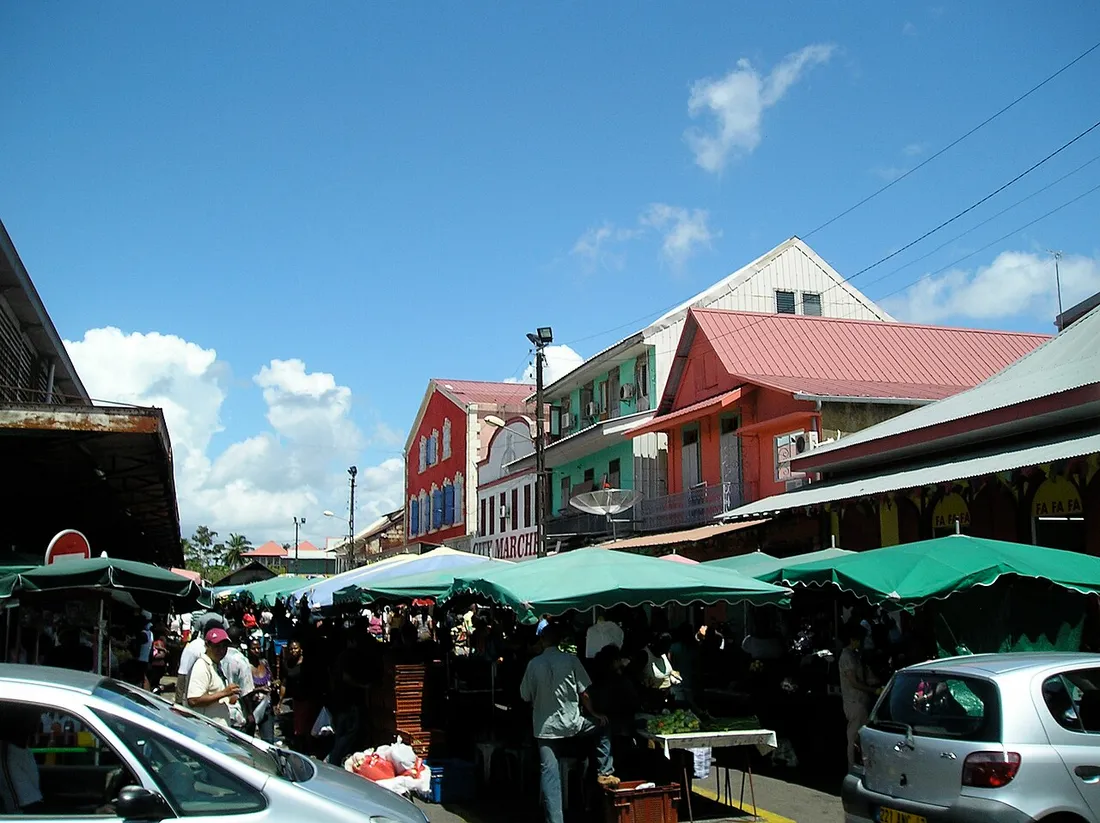 Vue du marché de Cayenne en Guyane avec ses parasols verts, ses étals animés et les façades créoles colorées du bâtiment Cité Marché