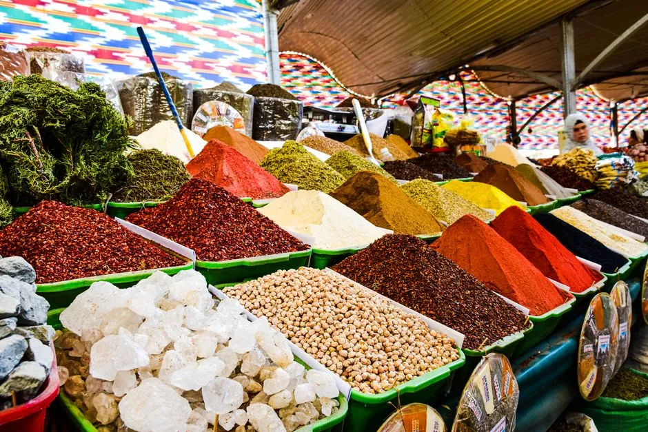 Etal de marché couvert présentant des montagnes d'épices colorées et de graines, evoquant les saveurs gourmandes et les bouillons du marché