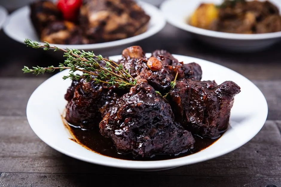 Plat creole antillais mijote dans une sauce caramelisee, garni d'une branche de thym frais, servi dans une assiette blanche