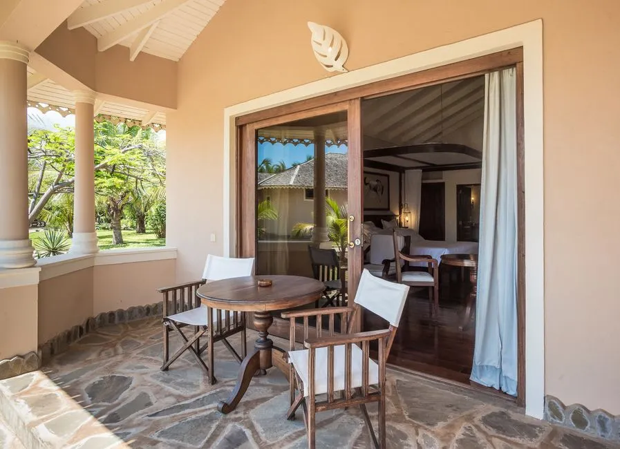 Terrasse confortable d'un hébergement tropical avec table, fauteuils et chambre ouverte sur le jardin, illustrant un séjour confort et accessible