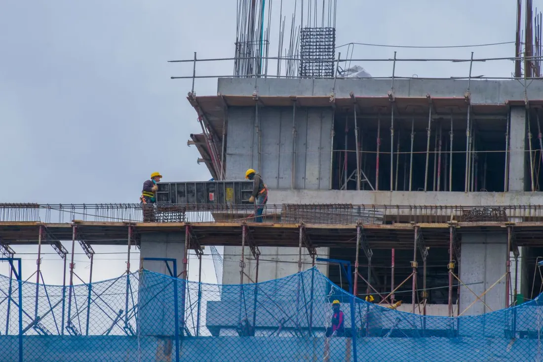 Ouvriers casqués sur les étages en béton armé d'un immeuble en construction, entourés d'étais, de coffrages et d'un filet de chantier bleu