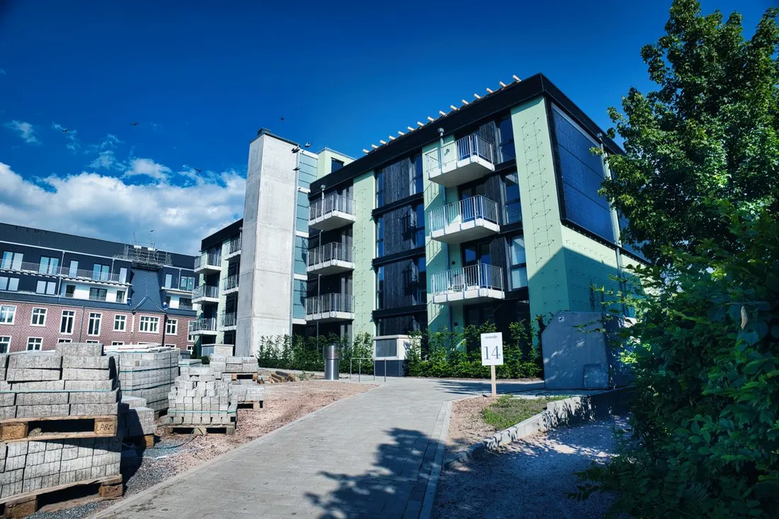 Petit immeuble résidentiel récent de trois étages avec balcons, vu depuis l'allée piétonne, des palettes de pavés encore stockées devant l'entrée