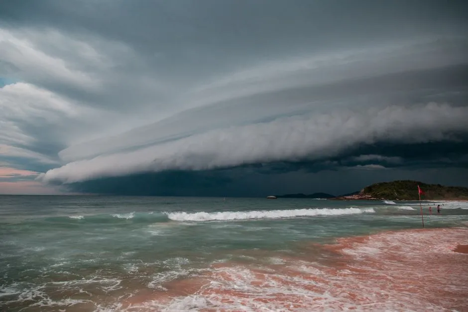 Front nuageux d'orage tropical au-dessus d'une plage avec vagues et houle qui déferlent, illustrant pluies et houle en Martinique