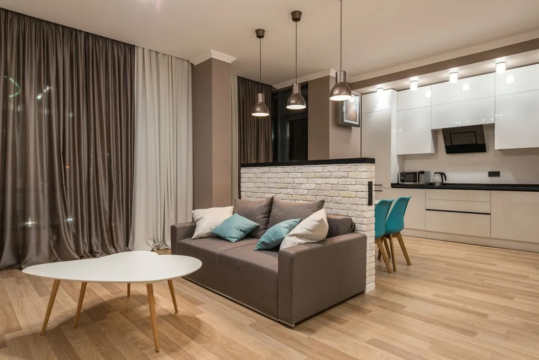 Sejour meuble et equipe avec canape, table basse et cuisine ouverte, typique d'un logement loue en meuble de tourisme