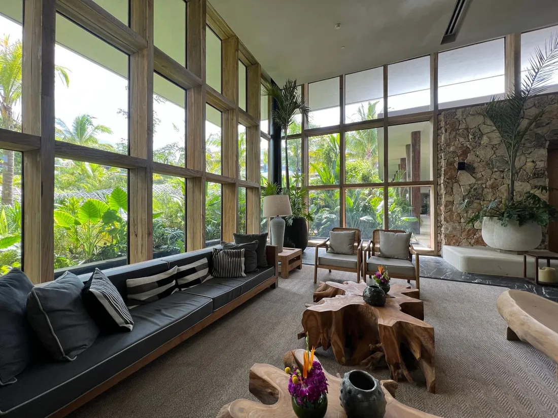Salon spacieux et meublé d'une location de vacances tropicale, avec baies vitrées ouvertes sur un jardin luxuriant
