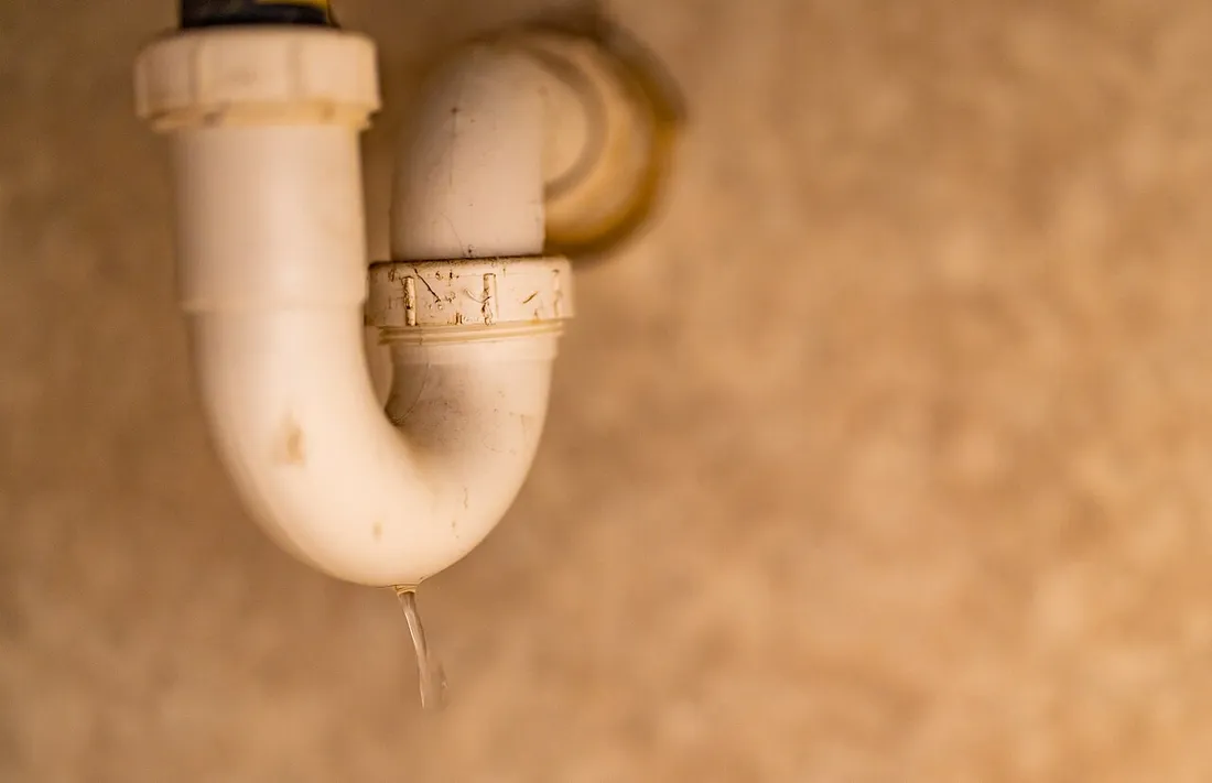 Siphon en PVC blanc sous un lavabo, une goutte d'eau suspendue à sa partie basse