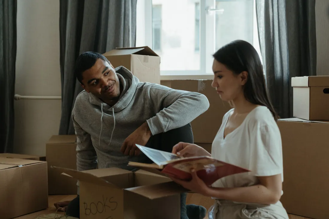 Couple deballant des cartons de livres dans le salon de son nouveau logement, ambiance d'emmenagement pour une rentree