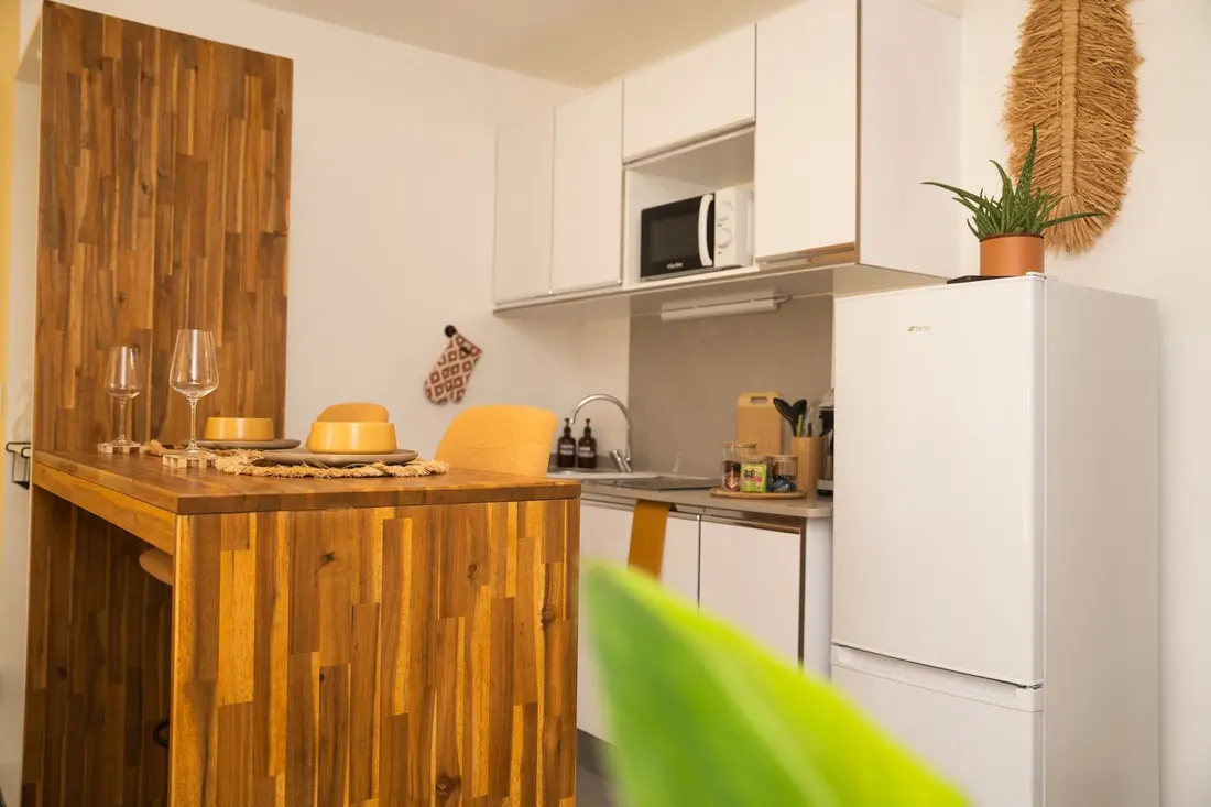 Kitchenette du Cocon Chic : bar en bois massif dressé pour deux, micro-ondes et réfrigérateur blancs