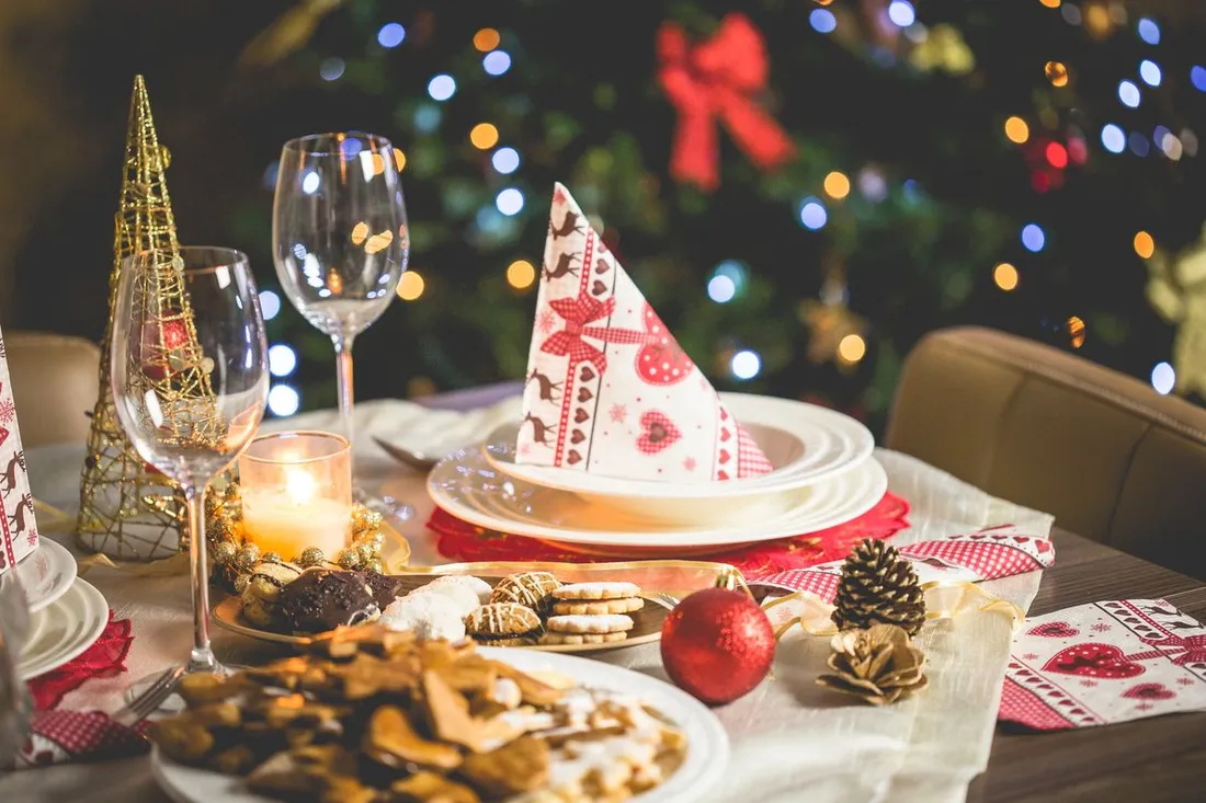 Table de Noël dressée avec bougie, verres et assiette de gâteaux devant un sapin illuminé