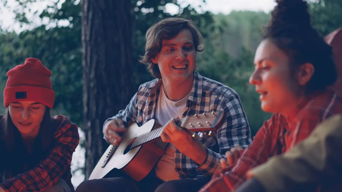 Trois amis chantent ensemble autour d'une guitare le soir, evoquant un chante Nwel guadeloupeen