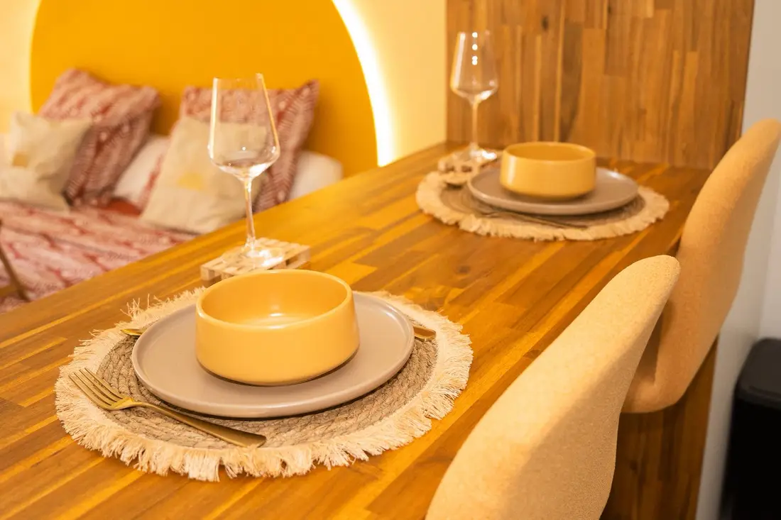 Table en bois dressée du Cocon Chic devant la tête de lit en arche jaune : bols, assiettes et verres à pied
