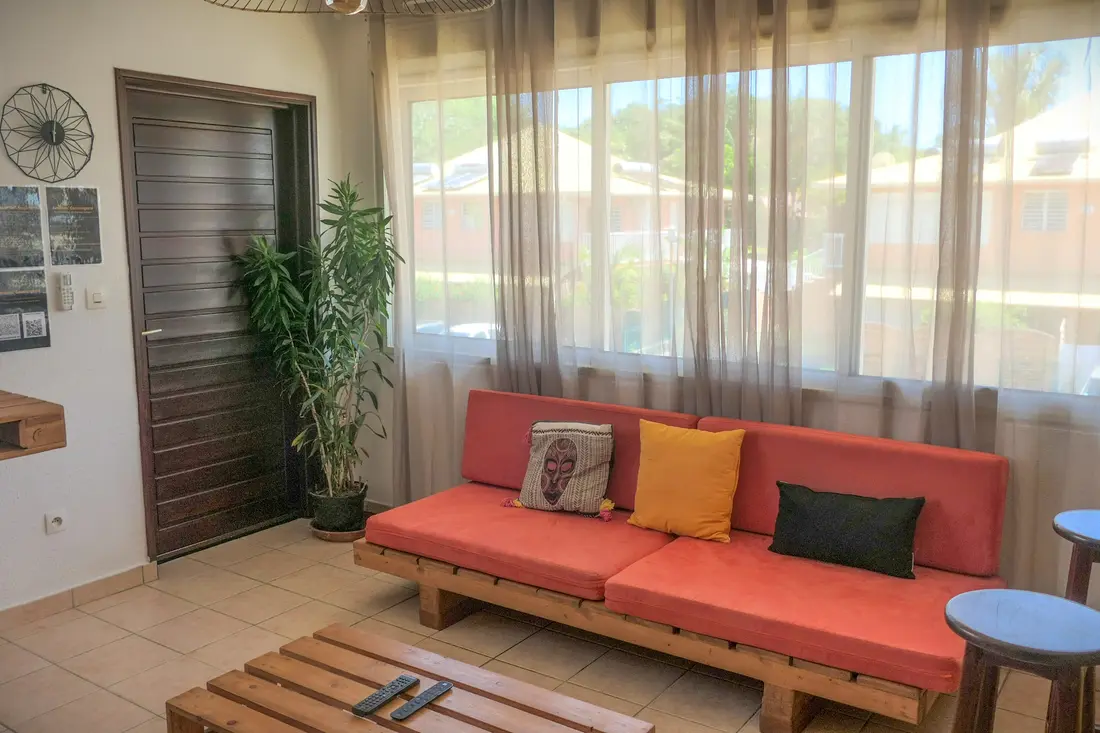 Salon d’un appartement Cayenne Chic : banquette corail en bois clair devant de grands voilages